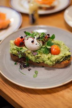 Fresh avocado toast topped with poached egg, cherry tomatoes, and microgreens in a Berlin cafe.