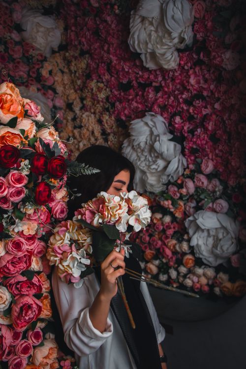 Free Woman holding bouquet of roses and hydrangeas against a rich floral wall. Stock Photo