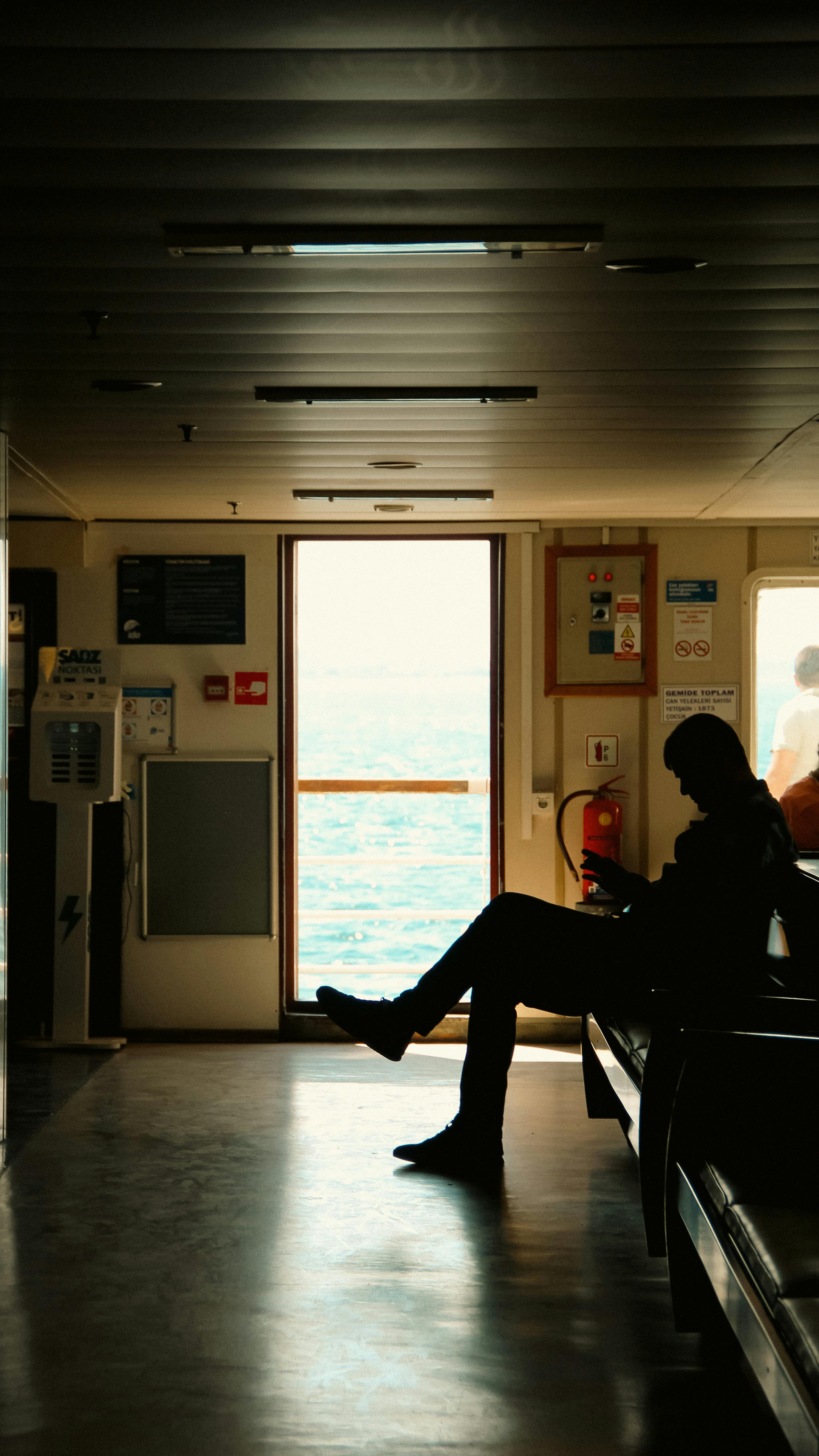 A silhouette of a man seated inside a ferry sailing in İstanbul, Türkiye, with a view of the sea.