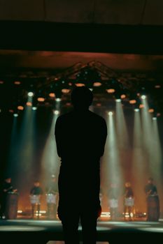 Silhouette of a man on stage with drummers and atmospheric lighting.