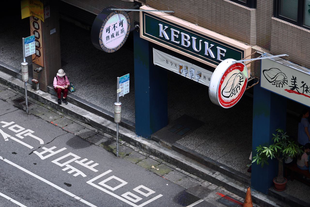 aerial view of a person waiting at a bus stop next to a store in taipe