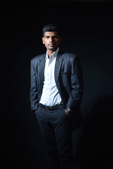 Portrait of a confident man in a black suit and white shirt against a black background, capturing elegance.