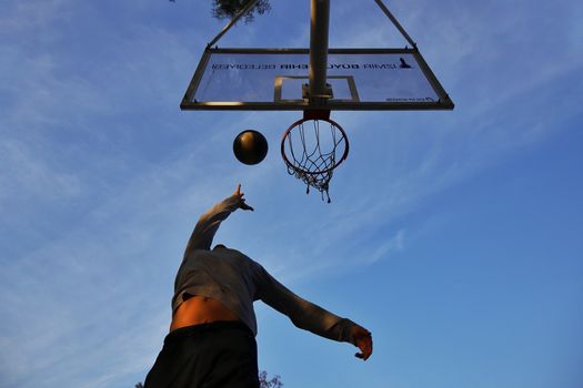 Athlete jumping to shoot a basketball with clear blue sky backdrop, captured from a low angle.