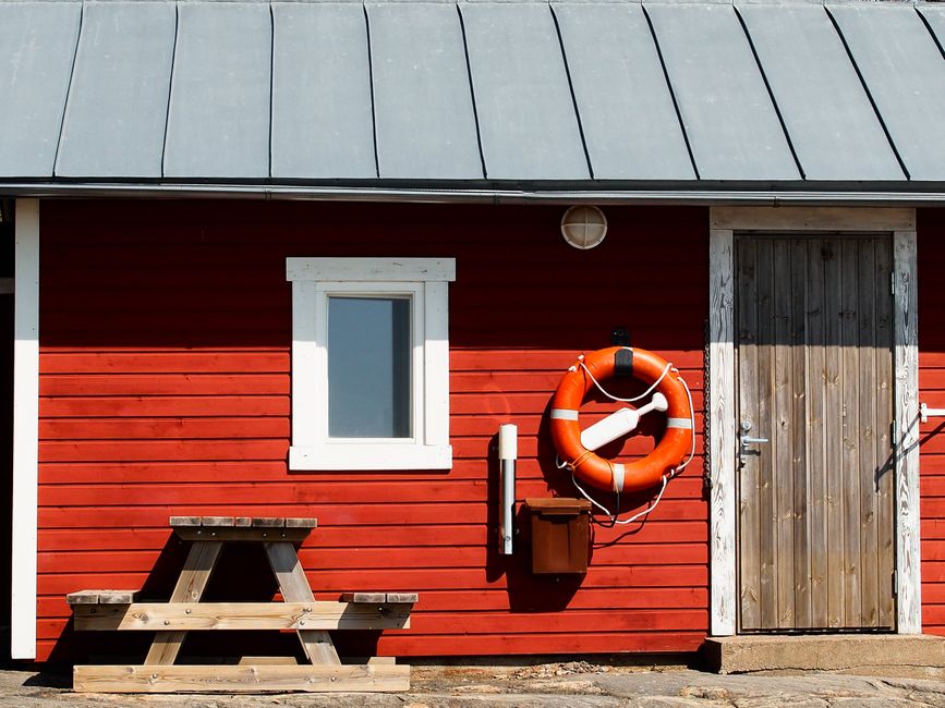 Red wooden lifeguard hut in Helsinki with life preserver and bench outside.