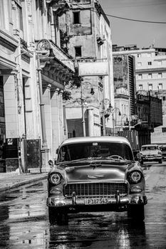 Classic vintage car parked on wet city street, captures timeless urban essence in black and white.