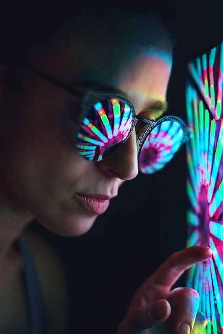 Close-up of a person wearing sunglasses reflecting neon lights in a dark setting.