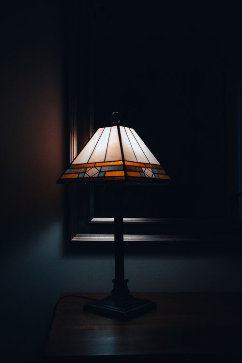 Free Elegant stained glass lamp casting warm light in a minimalist dark setting. Perfect for classic interior design. Stock Photo