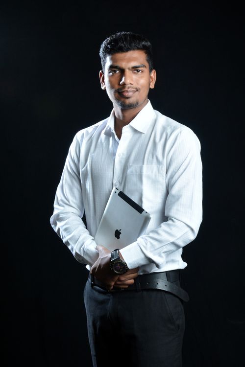Free A fashionable portrait of an adult man in a white shirt holding a tablet, standing against a black background. Stock Photo