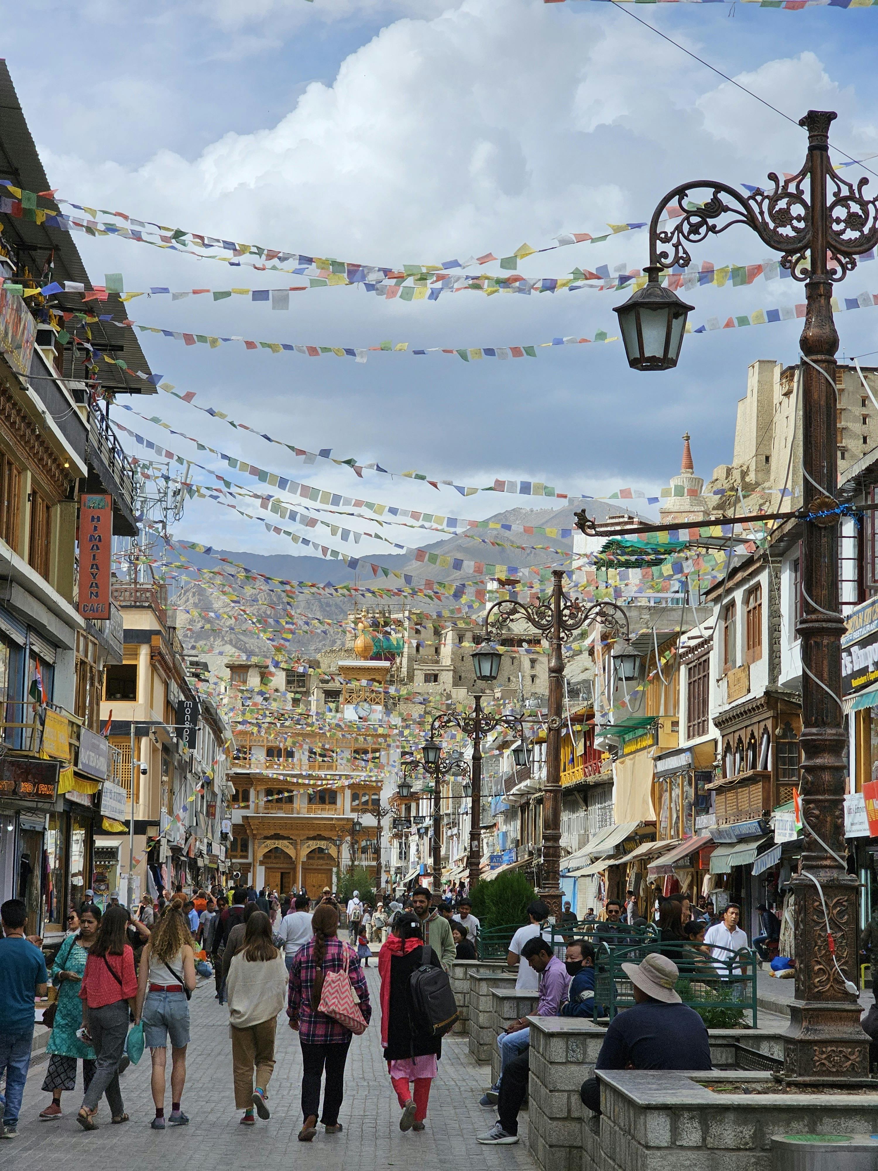 Vibrant market street in Leh, Ladakh with people and Tibetan prayer flags.