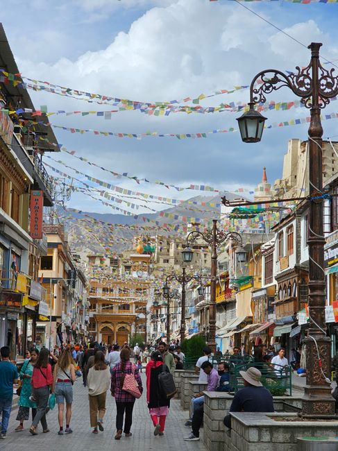 Vibrant market street in Leh, Ladakh with people and Tibetan prayer flags.