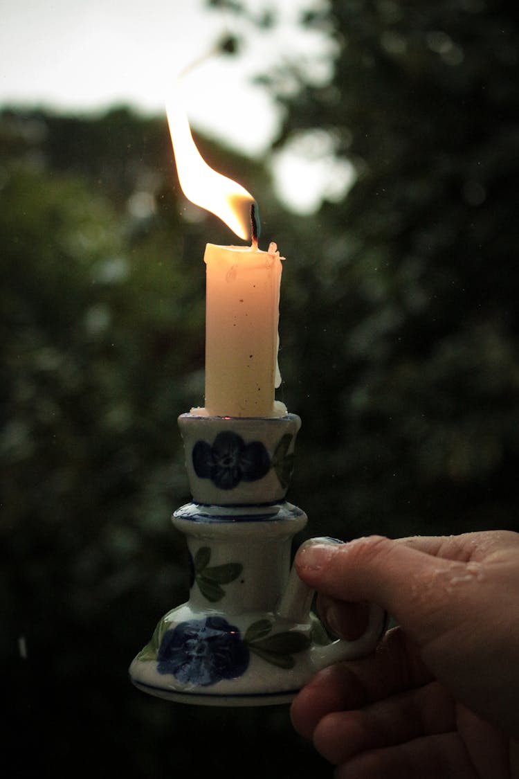 Holding A Porcelain Candlestick With A Lit Candle In The Rain