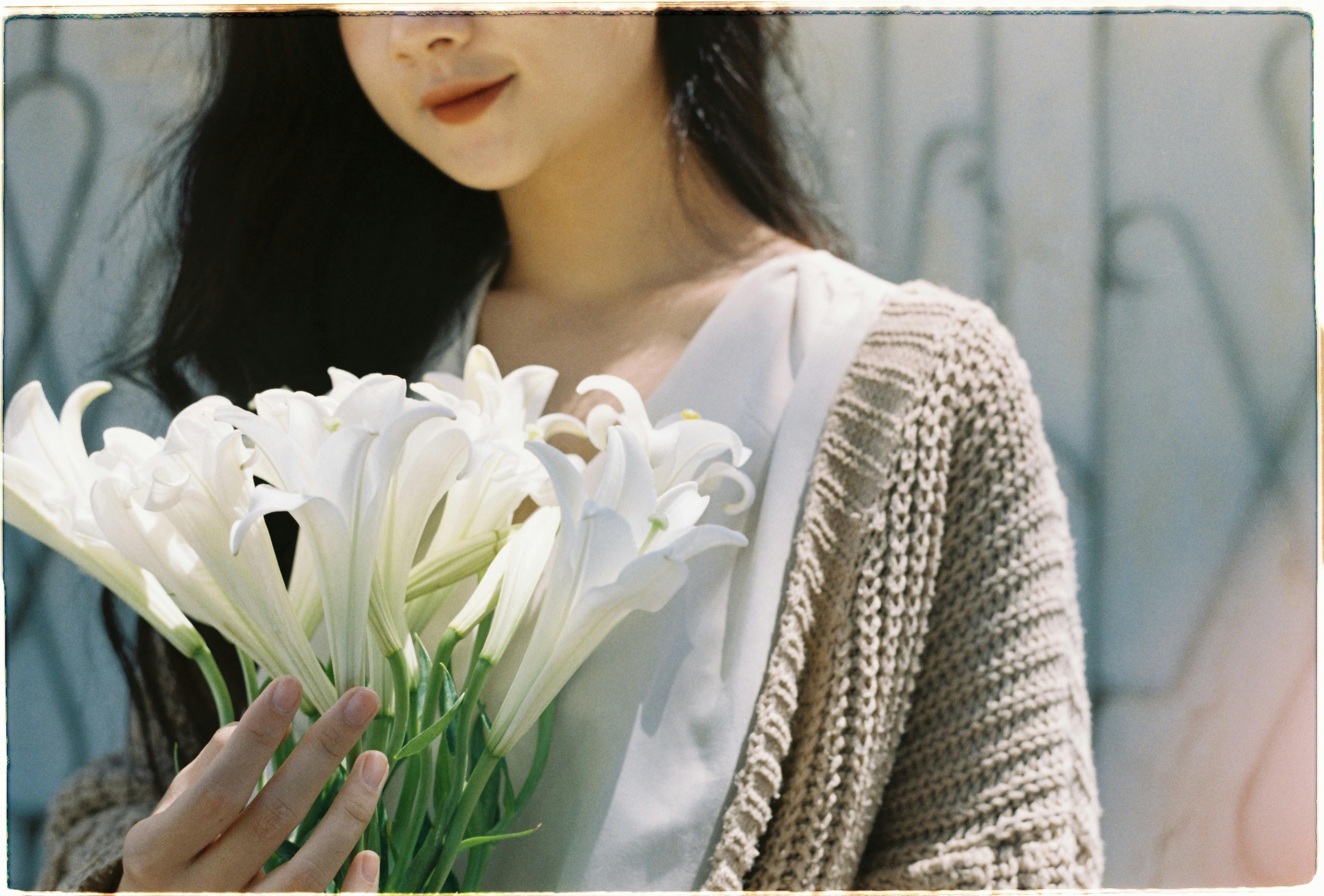 A woman in a cardigan gracefully holds a bouquet of white lilies, creating a serene summer scene.
