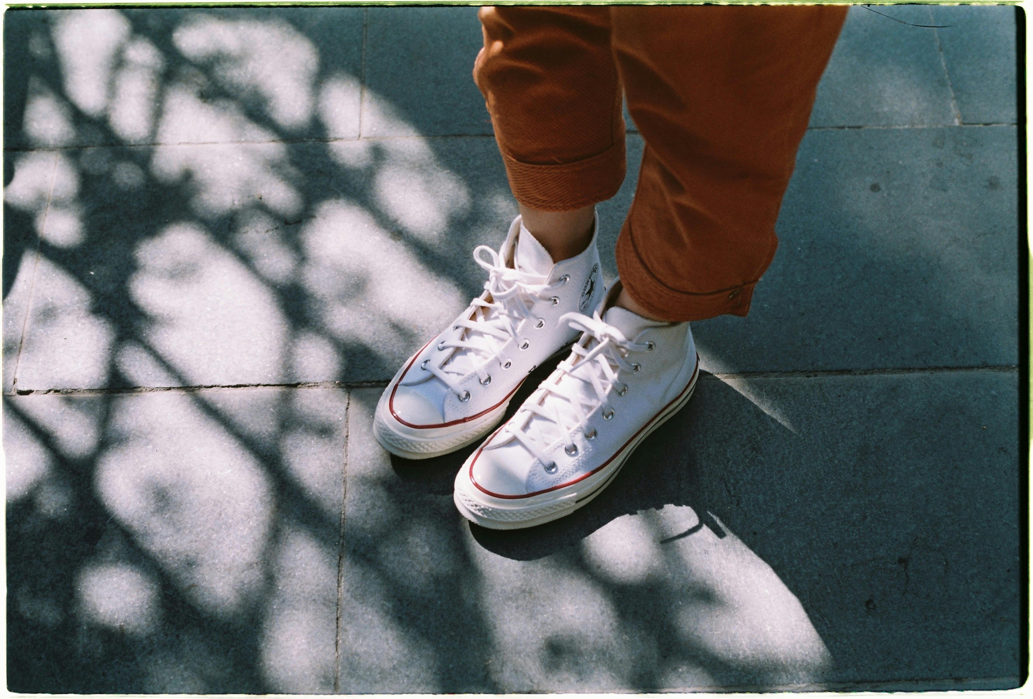Close-up of white sneakers on pavement with shadows, showcasing a casual fashion style.