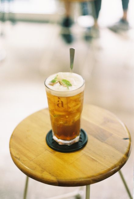 A tall glass of iced tea with mint on a rustic wooden table in a cafe setting.