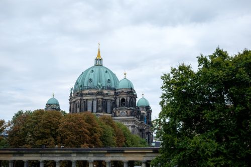 Free Berlin Cathedral with its iconic domes framed by lush trees under an overcast sky. Stock Photo