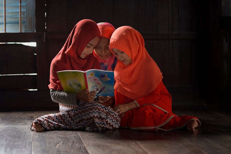 Little Girls Sitting On The Floor And Looking At A Book