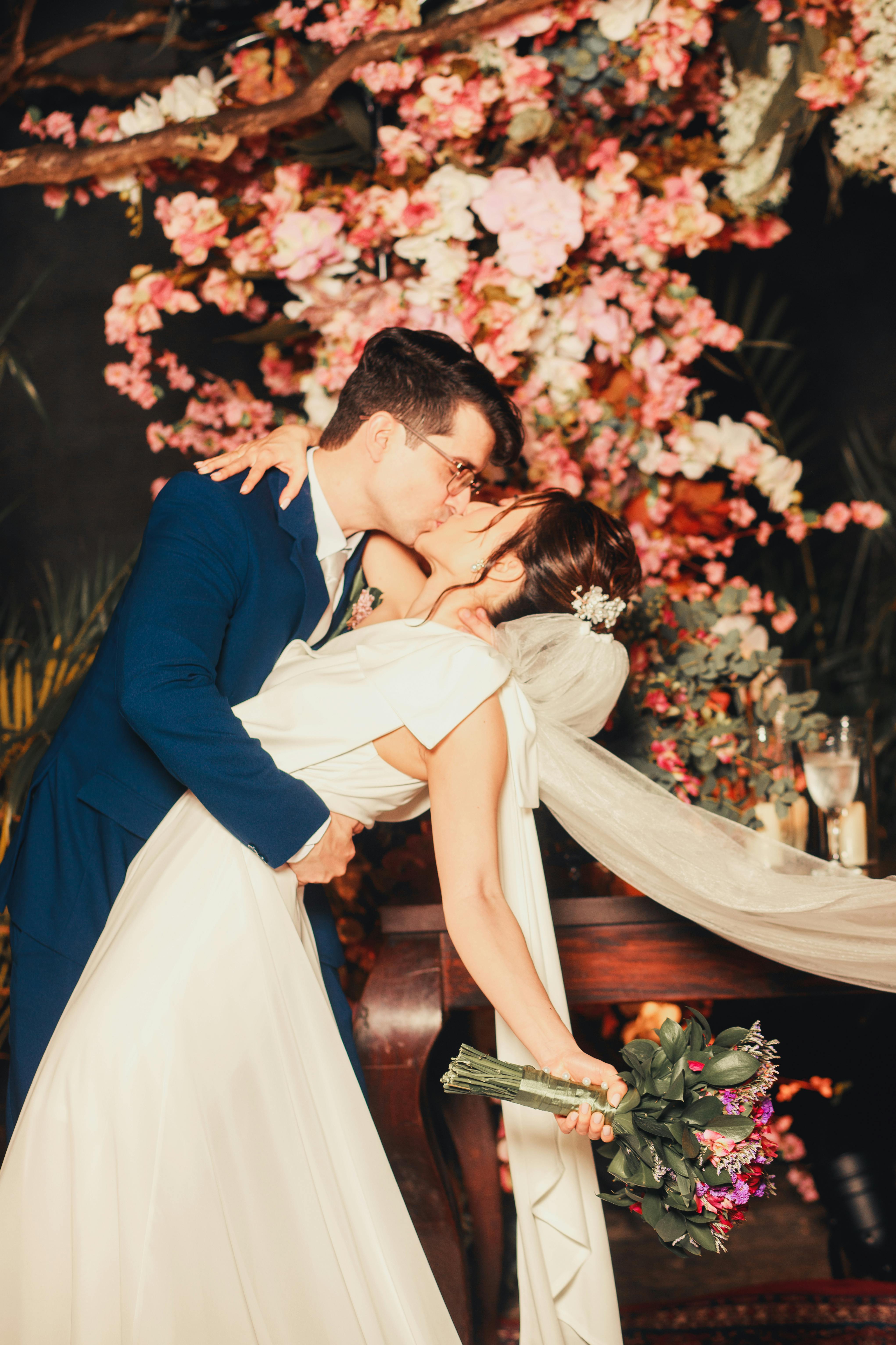 Bride and groom share a kiss under cherry blossoms, capturing intimate wedding moments.