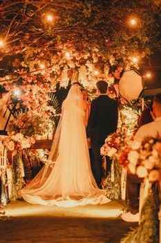 A beautifully illuminated outdoor wedding ceremony at night with bride and groom.