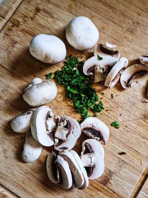 Free Sliced white mushrooms and green herbs displayed on a wooden cutting board, perfect for cooking inspiration. Stock Photo