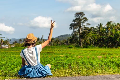 Free Woman Sitting Near Grass Field Showing Peace Hand Sign Stock Photo