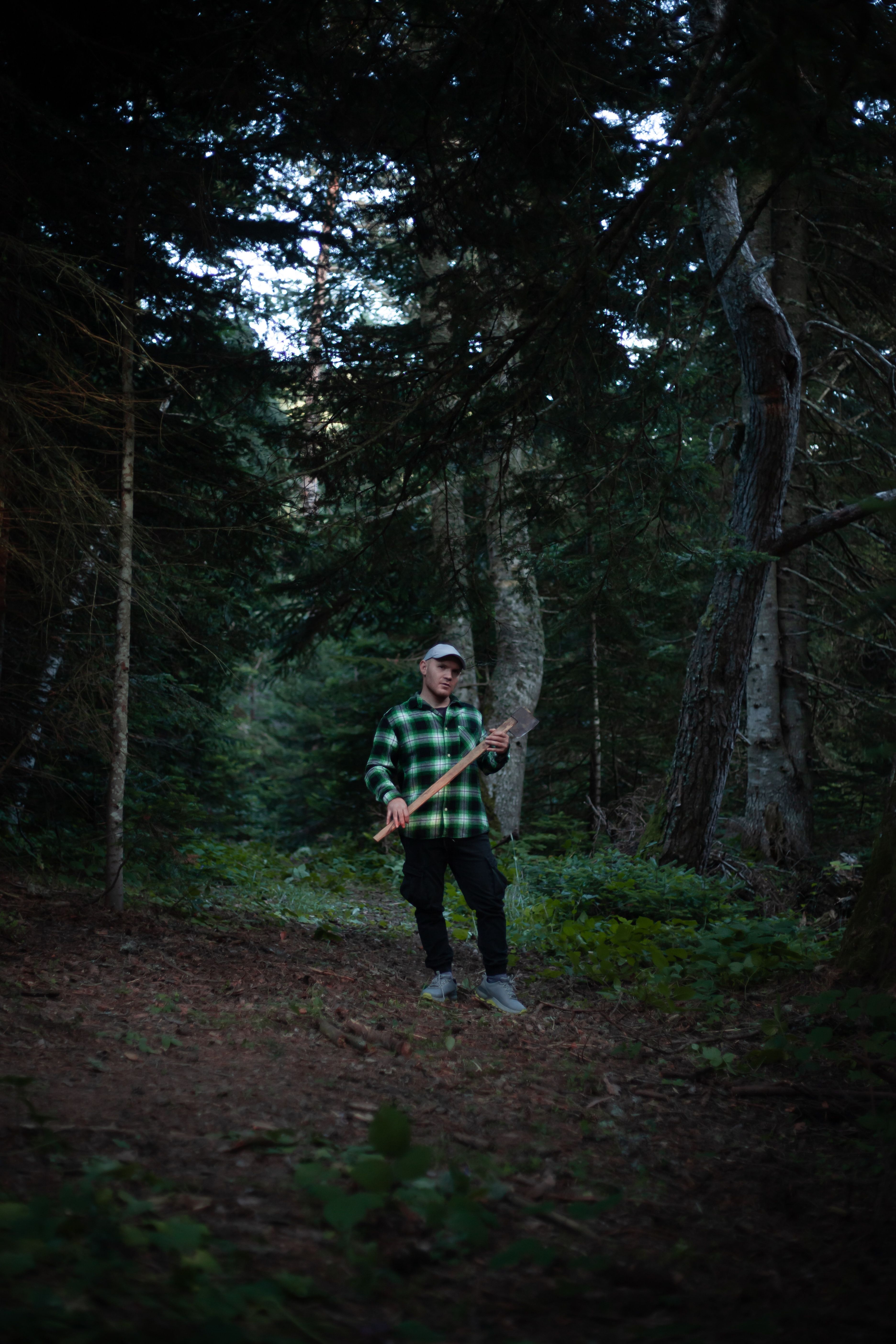 A man in a forest holding a baseball bat, surrounded by lush trees.