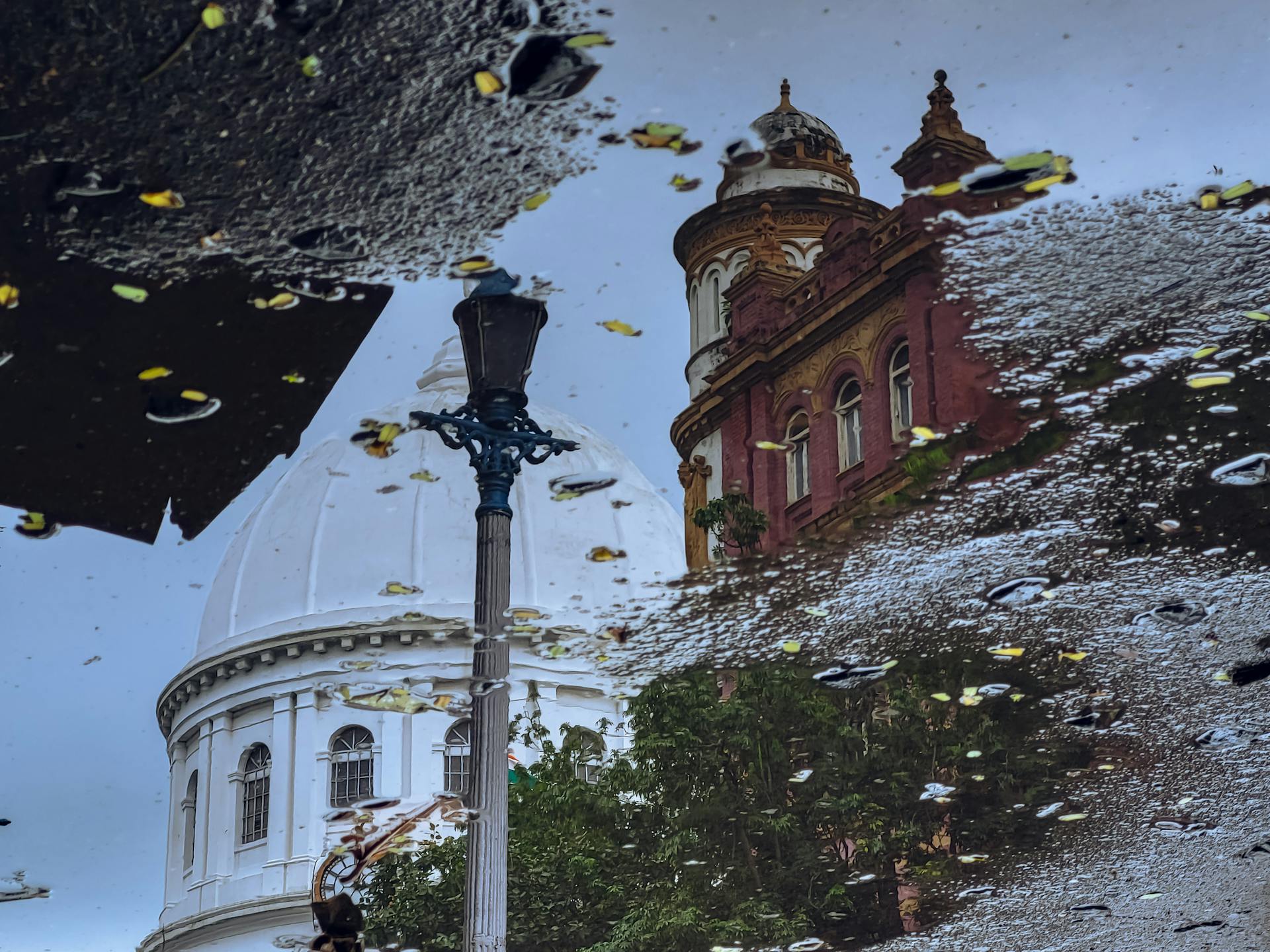 Capture of historical architecture's reflection in a Kolkata rain puddle with street lamp.