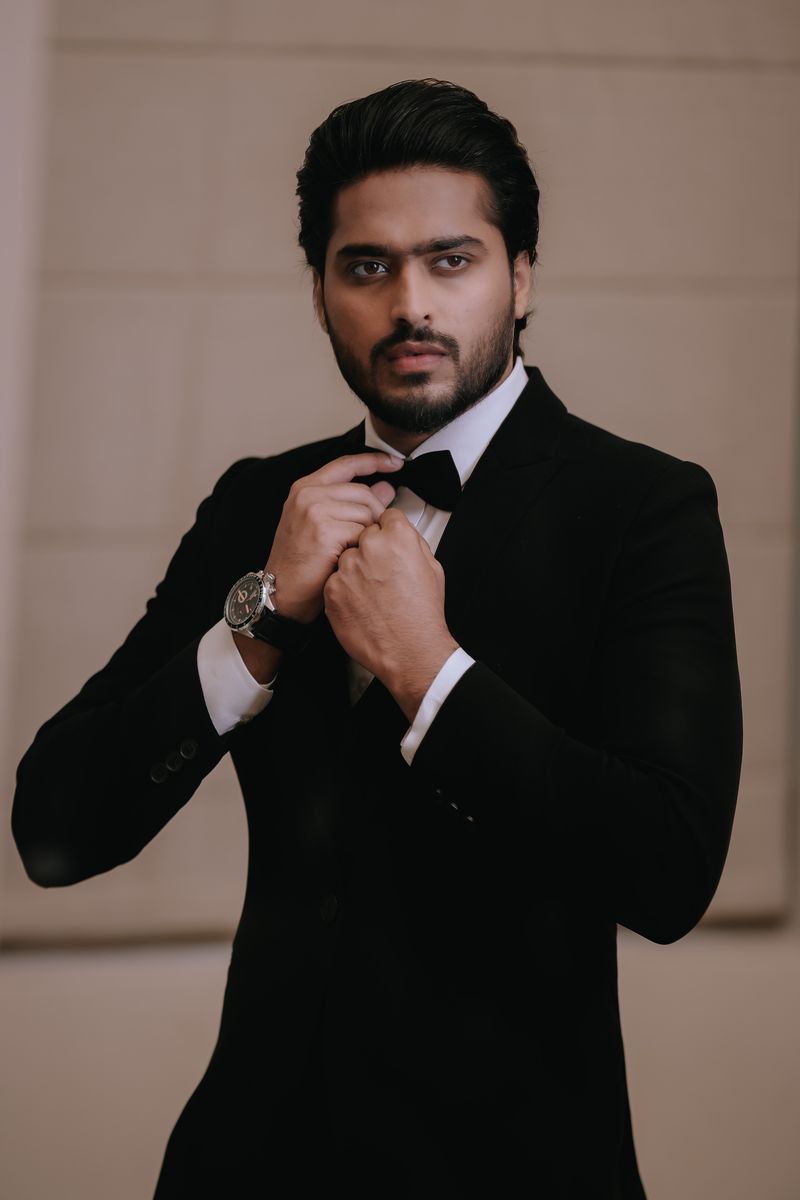 Groom in black tuxedo adjusting his bow tie