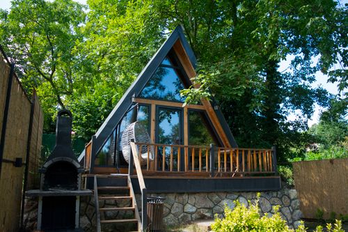 Free A charming A-frame cabin nestled among lush trees featuring a stone patio and outdoor stove. Stock Photo
