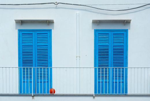 A minimalist scene of blue shutters and a white balcony with a red ball, conveying a vibrant urban aesthetic.