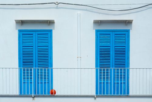 Free A minimalist scene of blue shutters and a white balcony with a red ball, conveying a vibrant urban aesthetic. Stock Photo