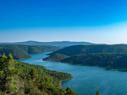 Free Breathtaking view of Krka River with lush hills under a clear blue sky in Skradin, Croatia. Stock Photo