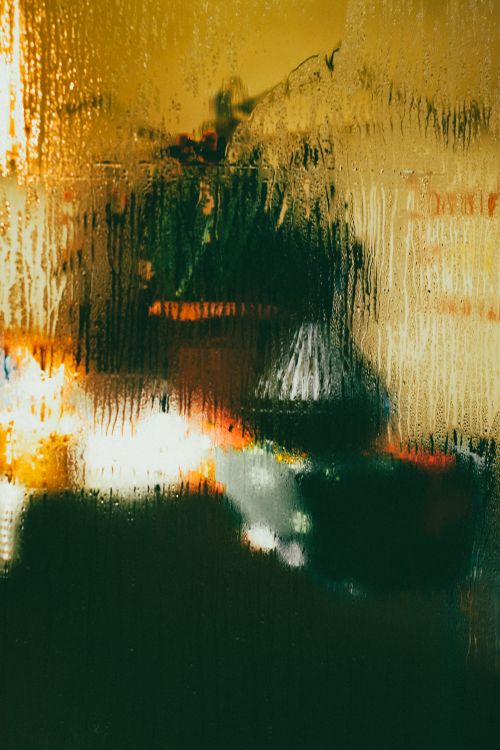 Free A moody abstract view of a city through wet glass, capturing rain-soaked streets and blurred lights. Stock Photo