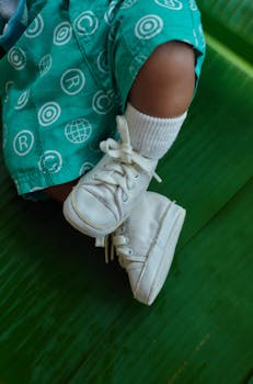 Close-up of a child's feet in white sneakers on a green background, conveying playfulness and youth.