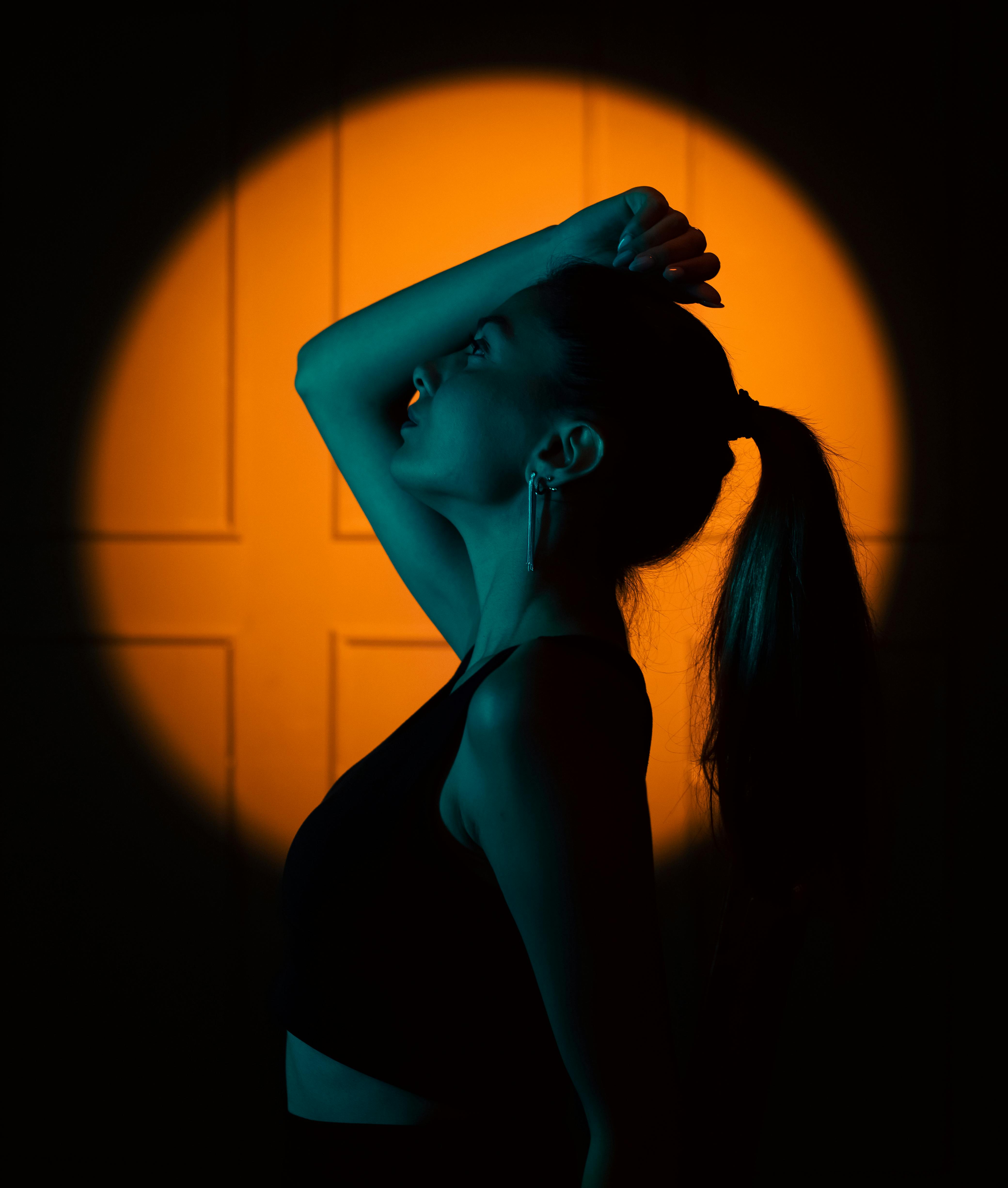 Artistic silhouette of a woman posing against orange spotlight, conveying mystery and elegance.