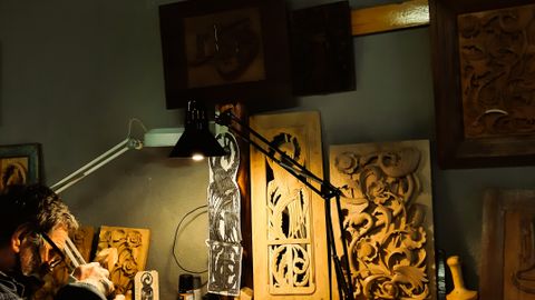 Intricate wood carving by a skilled artisan in a detailed workshop scene.