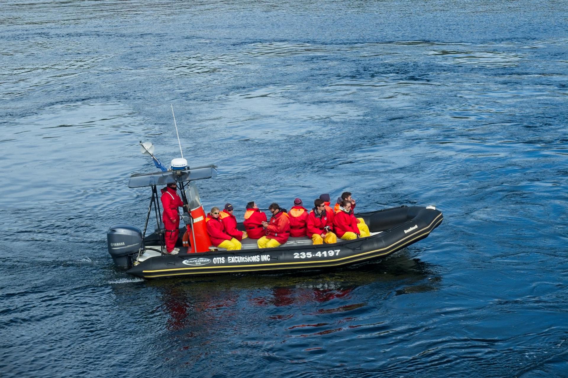 A group in red and yellow waterproof gear on an inflatable boat on a wide waterway.