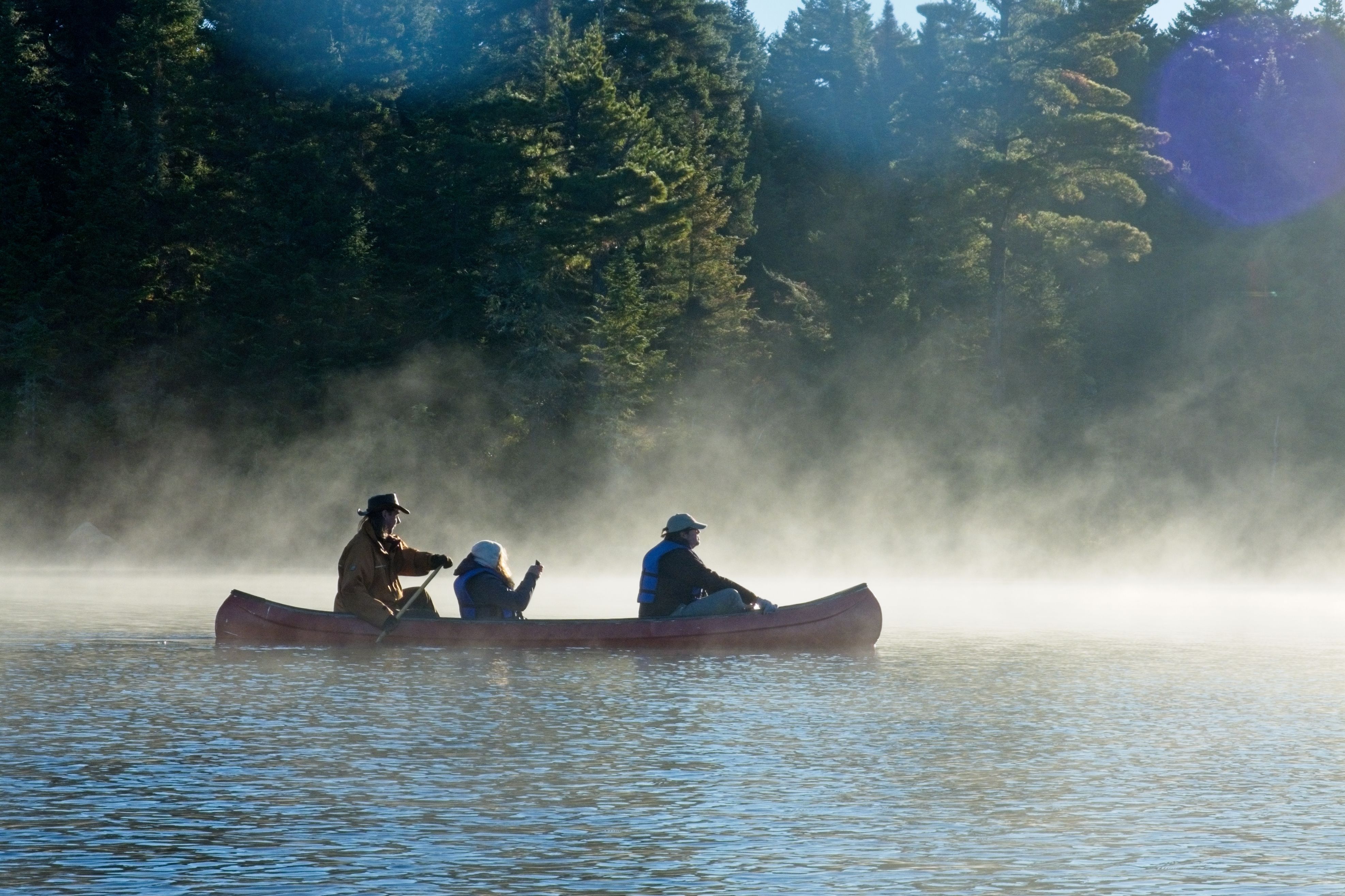 A scenic canoe trip with people in a misty river surrounded by a dense forest.