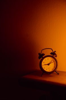 A vintage alarm clock on a wooden shelf lit by warm light, evoking nostalgia.