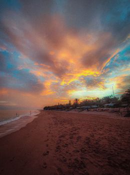 Tropical beach during a vibrant sunset with colorful sky and calm sea.