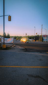 A yellow vintage van drives on an empty city street at dusk, surrounded by traffic lights and trees.