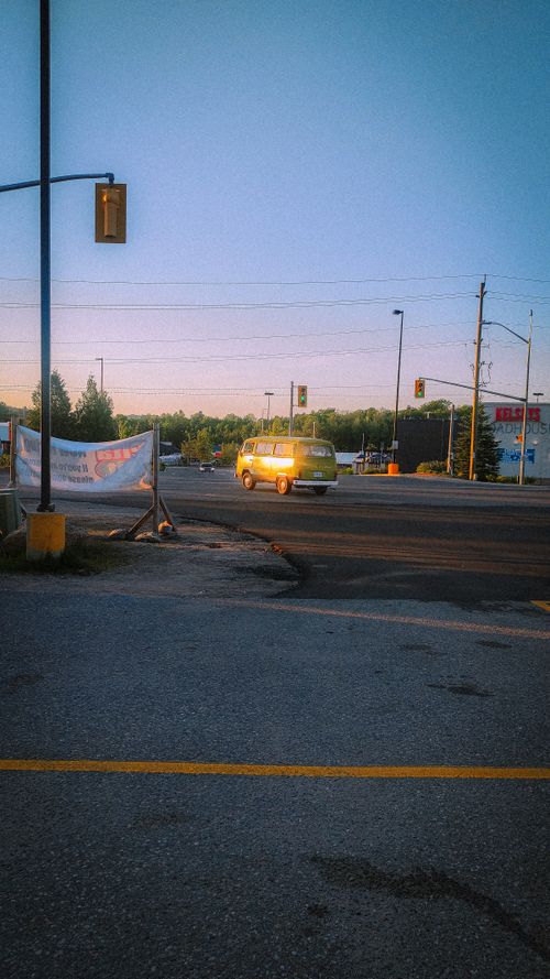 Free A yellow vintage van drives on an empty city street at dusk, surrounded by traffic lights and trees. Stock Photo