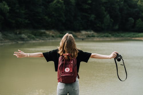 Free Back View of Woman Standing with Arms Stretched with Lake behind Stock Photo