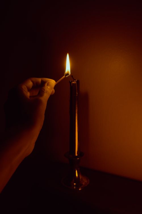 Free A hand holding a match to light a candle in dim surroundings, creating a warm ambiance. Stock Photo