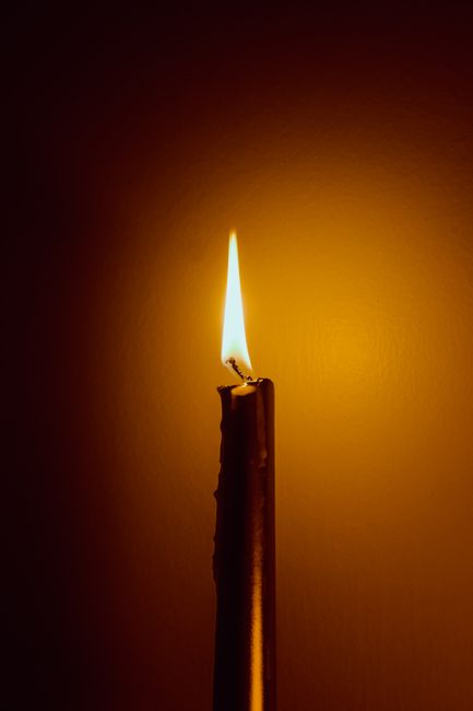 Close-up of a single candle in the dark casting a warm, soothing glow.