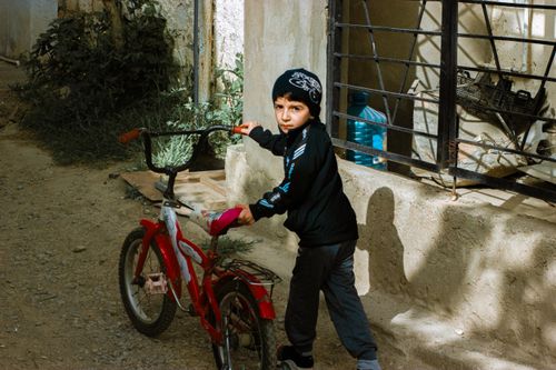 Free A young boy stands with a bicycle in a dimly lit urban alleyway, wearing a winter cap. Stock Photo
