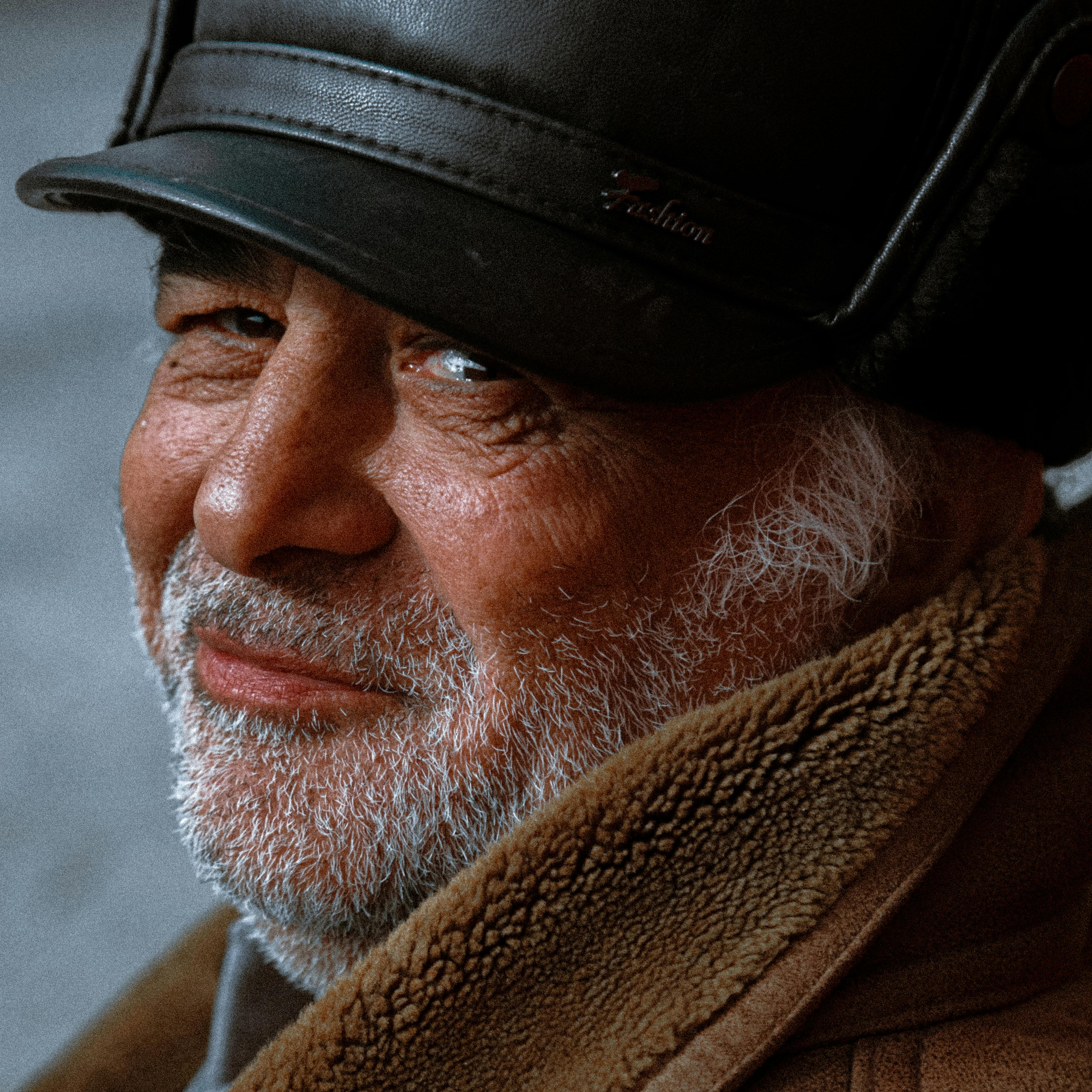 A thoughtful portrait capturing an elderly man with a beard wearing a leather hat and coat.