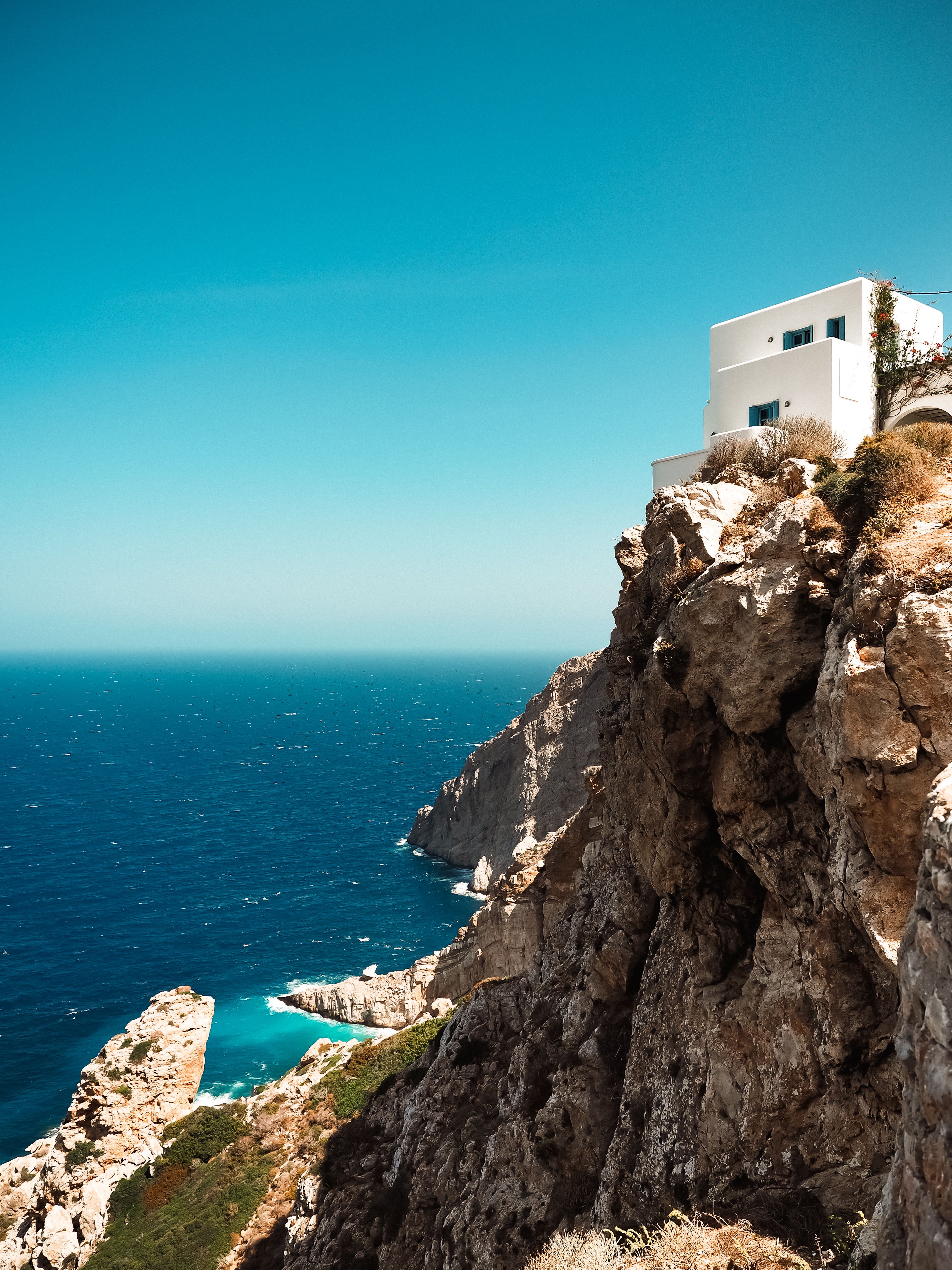 Idyllic white house perched on a Greek cliff with ocean view under clear sky.