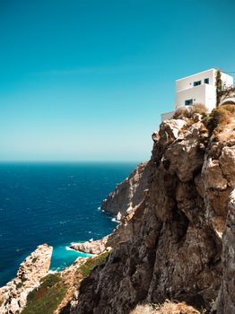 Idyllic white house perched on a Greek cliff with ocean view under clear sky.