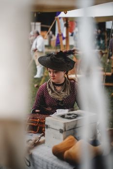 Woman in historical attire participates in a reenactment event under a tent.