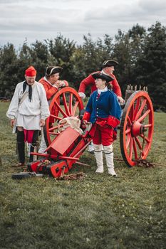 Group of men in 19th-century military costumes with cannons in a reenactment field.